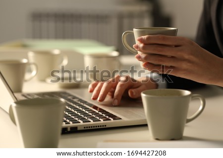 Close up of overworked executive woman hands working late hours wih multiple coffee cups in the office at night