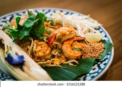 Close up of Pad Thai. Thai style fried noodles with shrimps prawns and vegetables beautifully decorated in plate on wooden table. Traditional Thai food menu for restaurant. Copy space. Asian food.