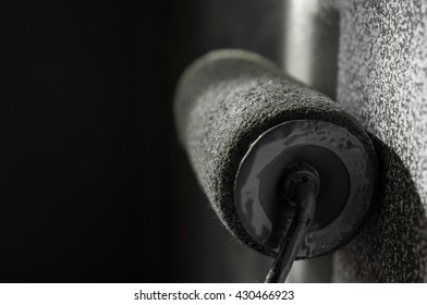 Close up of paint roller applying grey paint on white wall.