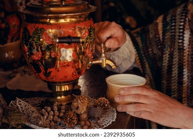 Close up of a painted samovar standing against the background of a brown curtain.
