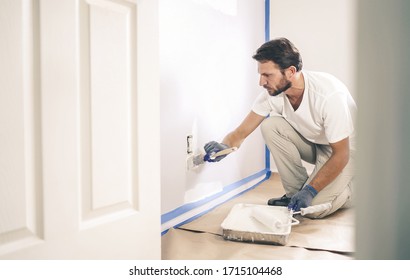 Nahaufnahme eines Malers mit Handschuhen, die die Wand um die Steckdose malen.
