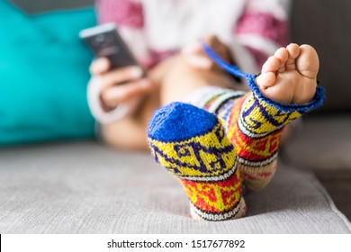 Close Up Of Pair Of Feet Outside A Broken Handmade Coloured Funny Socks - Concept Of Different Lifestyle And Real Life At Home - Modern Phone In Background