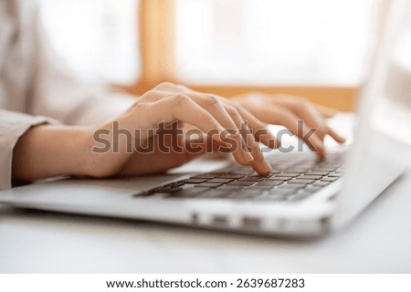 Close up of a pair of hands typing both hands on laptop's keyboard at white table beside glass wall in the cafe. Working or Study, Chilling Outside.