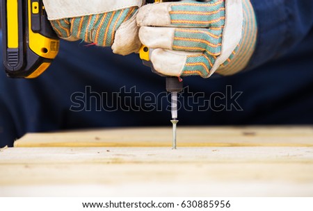 Close up of pair of hands in work gloves drilling a screw into wood with an electric drill