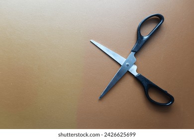 close up of a pair of opened scissors on a brown leather background on the right in a 