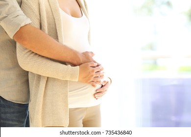 Close up of parents hands touching pregnant belly at home