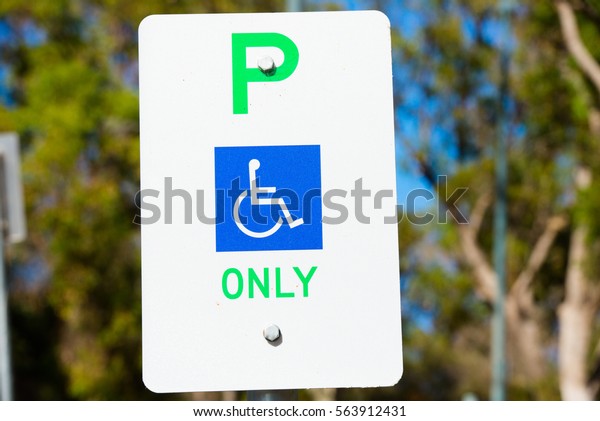 Close up parking sign reservation for disabled car
driver or person, wheelchair symbol on blue, outdoor blurred
background, copy space.