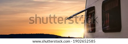 Close up part of camper van or caravan truck with window open parking at view point stop. Relax scene with sunset sky. Banner and web header ratio size.