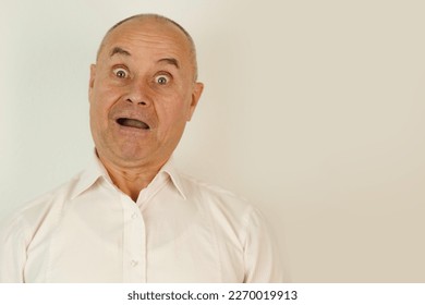 close up part of funny male face, goggle eyes, mature man 60 years old, senior looks in mirror at his reflection, examines face, skin, wrinkles, jokingly grimaced, concept of baldness and hair loss