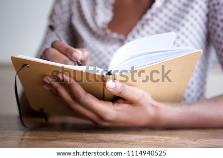 Close up partial portrait of black female author at home writing in journal