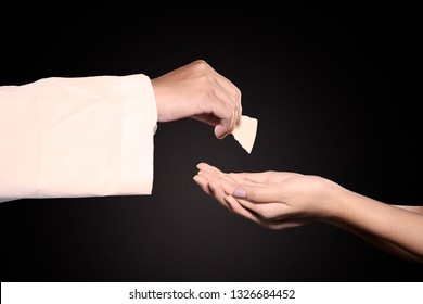 Close Up Of Pastor Giving First Communion Bread On Woman Hands In Dark Background