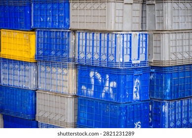 Close up pattern of blue, gray, and yellow plastic crates stacked neatly at a fish market or industrial warehouse. Concept for logistics, storage, seafood industry, container, and pattern background.