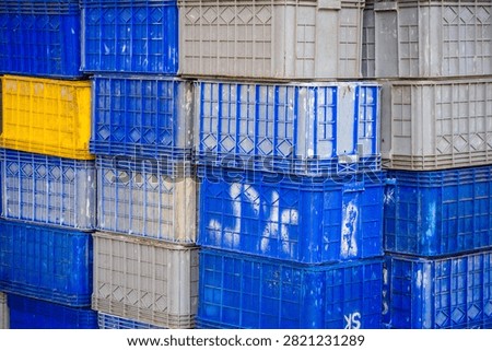 Close up pattern of blue, gray, and yellow plastic crates stacked neatly at a fish market or industrial warehouse. Concept for logistics, storage, seafood industry, container, and pattern background.