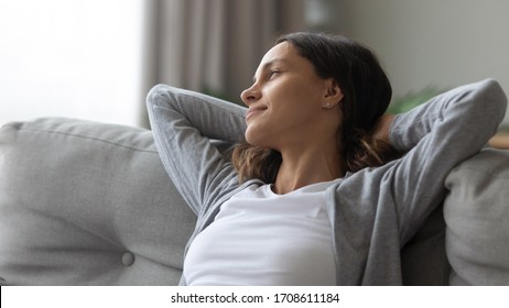 Close up peaceful young woman resting on couch, looking to aside out window, dreaming about good future and planning new day, calm serene beautiful girl relaxing on cozy sofa at home