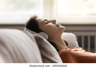 Close up peaceful young woman wearing headphones listening to music with closed eyes, leaning back on cozy couch at home, mindful calm sleepy attractive female enjoying favorite song, leisure time - Powered by Shutterstock