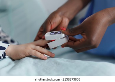 Close Up Of Pediatric Clinic Nurse Measuring Sick Child Oxygen Levels While In Patient Recovery Ward. Hospital Staff Checking Sick Little Girl Oxygen Level While Laying Relaxed On Patient Medical Bed.