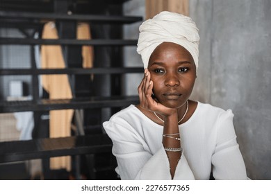 Close up of pensive African young woman in white turban sitting on stairs leans on hand staring aside puzzled by difficulties and financial crisis. Thoughtful African American girl unhappy at home. - Powered by Shutterstock