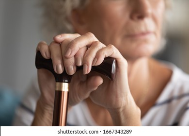 Close up of pensive mature disabled woman with walking stick lost in thoughts feeling abandoned lonely at home, sad old 60s grandmother with cane thinking mourning indoors, elderly solitude concept