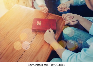 Close Up Of  People Group Holding Hand And Pray Together Over A Blurred Holy Bible On Wooden Table, Christian Fellowship  Or Praying Meeting In Home Concept With Copy Space