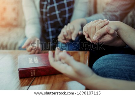 Close up of  people group holding a hand and pray together over a blurred holy bible on wooden table, Christian fellowship  or praying meeting in home concept with copy space