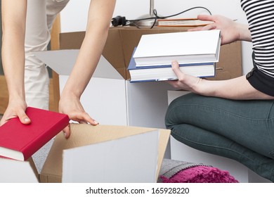 A close up of people packing books into a cardboard box