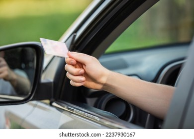 Close up person hand out of the car window holding the driver license as shows it to the police officer for control - Shutterstock ID 2237930167