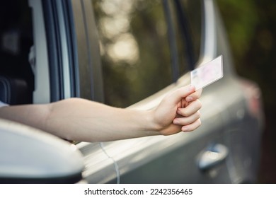 Close up person hand out of the car window holding the driver license as shows it to the police officer for control - Shutterstock ID 2242356465
