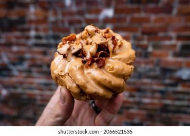 A Close Up Of A Person Holding A Bacon Maple Donut.