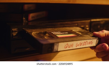 Close Up of a Person Inserting a VHS Cassette in a Player with Nostalgic Wedding Footage from Home Video Camera. Retro Nineties Technology Concept. Old VCR with Shallow Depth of Field and Bokeh.