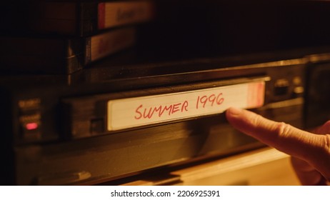 Close Up of a Person Inserting a VHS Cassette in a Player with Nostalgic Summer Footage from Home Video Camera. Retro Nineties Technology Concept. Old VCR with Shallow Depth of Field and Bokeh.