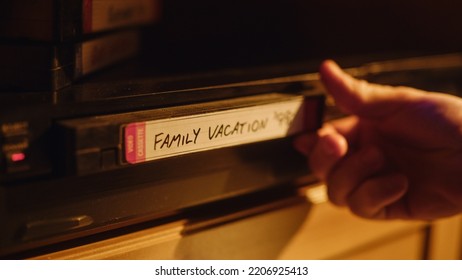 Close Up Of A Person Inserting A VHS Cassette In A Player With Happy And Nostalgic Vacation Footage From Home Video Camera. Retro Nineties Technology. Old VCR With Shallow Depth Of Field And Bokeh.