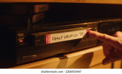 Close Up Of A Person Inserting A VHS Cassette In A Player With Nostalgic Vacation Footage From Home Video Camera. Retro Nineties Technology. Old VCR With Shallow Depth Of Field And Bokeh.