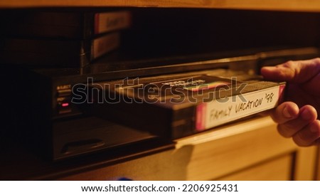 Close Up of a Person Inserting a VHS Cassette in a Player with Nostalgic Vacation Footage from Home Video Camera. Retro Nineties Technology Concept. Old VCR with Shallow Depth of Field and Bokeh.