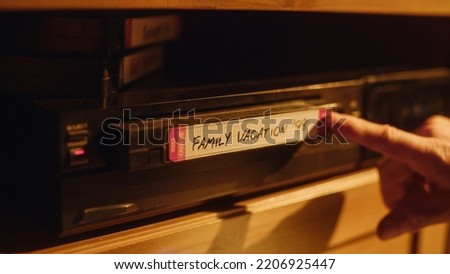 Close Up of a Person Inserting a VHS Cassette in a Player with Nostalgic Vacation Footage from Home Video Camera. Retro Nineties Technology. Old VCR with Shallow Depth of Field and Bokeh.
