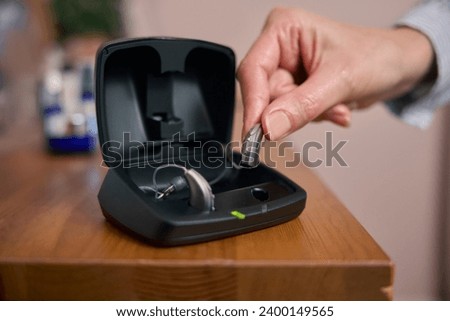 Close Up Of Person Picking Up Wireless Hearing Aid Or Device From Charging Case At Home