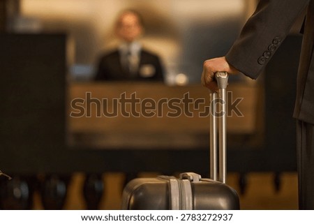 Close up of person pulling suitcase while checking in at hotel reception, representing business travel and hospitality. Ideal for tourism, corporate trip, lodging ads