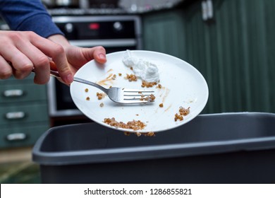 Close Up Of A Person Throwing From A Plate The Leftover Of Buckwheat To The Trash Bin. Scraping Food Waste