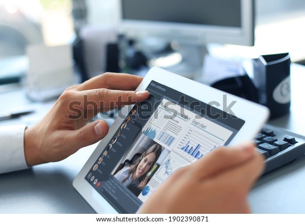 Close up of person video conferencing with\
colleagues on digital tablet, analyzing financial statistics\
displayed on the laptop\
screen.