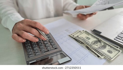 Close Up of a Person's Hand Using a Calculator to Calculate Expenses With a Stack of Cash and Papers