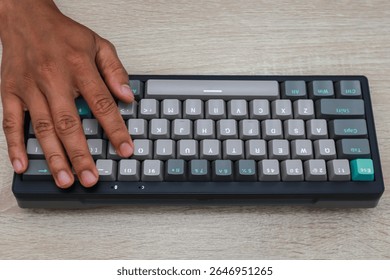 Close up of a person's hand using a compact, gray and teal mechanical keyboard on a light colored