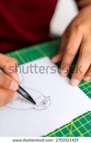 Close up of a person's hands creating a bird illustration with a fineliner pen on paper, focusing on artistic process