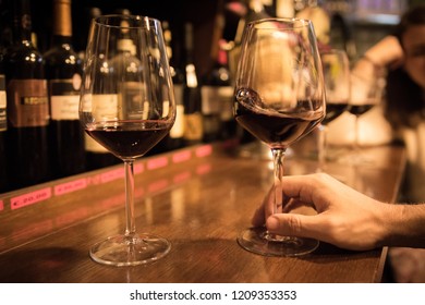 Close up perspective of crystal clear wine glass filled with red wine on wood counter top bar with blurry restaurant background scene