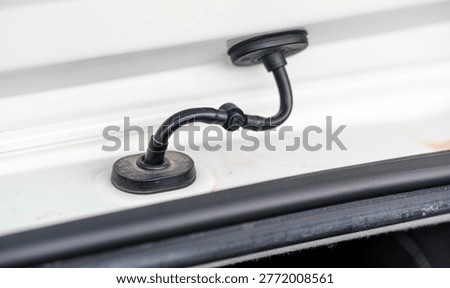 Close perspective highlighting the small flexible black rubber wiring tube bridging the electrical connection between the car body and the trunk lid on a white car