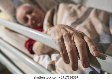 Close Up Pf Old Man's Hand On Bar Of Medical Bed. Senior Man Lying In Hospital