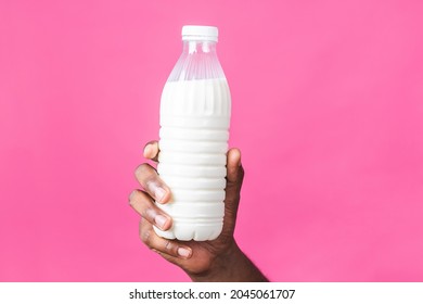 Close up photo of african american black man's hand holding bottle of milk isolated over pink background. Healthy food concept.