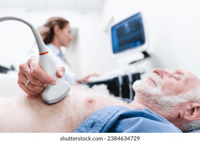 Close up photo of an aged male patient being examined with ultrasound scanner in the foreground and female doctor in the background. Internal organs sonography - Powered by Shutterstock