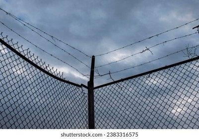 Close up photo of a barbed wire chain link fence against a dark stormy sky