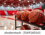 Close up photo of basketballs on storage rack inside of a gym with wood floors and red bleachers.
