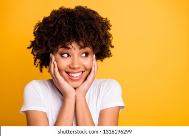 Close up photo beautiful amazing she her dark skin lady arms touch cheekbones look wondered empty space charming toothy smile wearing casual white t-shirt isolated yellow bright vivid background