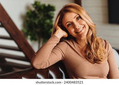 Close up photo of beautiful middle aged woman relaxing on sofa at home. Portrait of mature caucasian woman looking at camera. Unaltered beauty